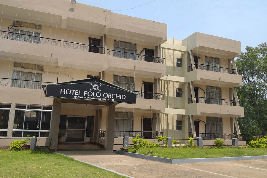 alt-text Hotel Polo Orchid facade with its sign, a neat lawn in front, and clear skies above.