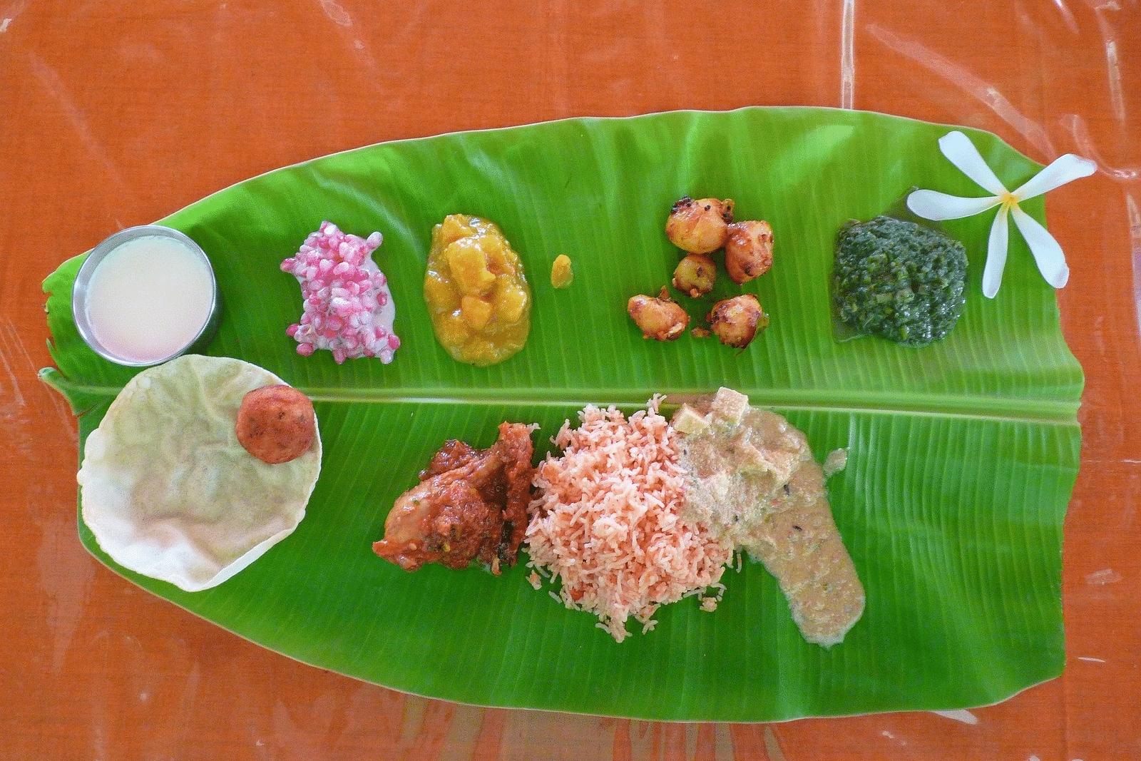 An aerial view of a banana leaf that is used as a plate with many items kept on it to consume.