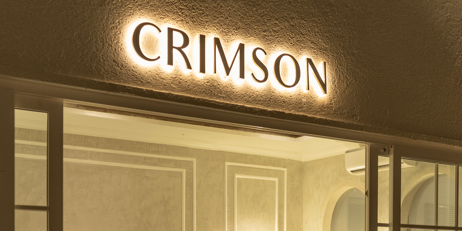 Night-time view of the crimson cafe interior with a person seated, featuring warm lighting and a checkered floor at Hotel Hukam's Lalit Mahal.