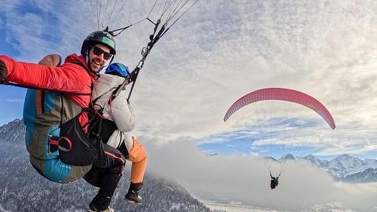 A paraglider in flight against a backdrop of snow-covered mountains and a clear sky, embodying the freedom of the sport.