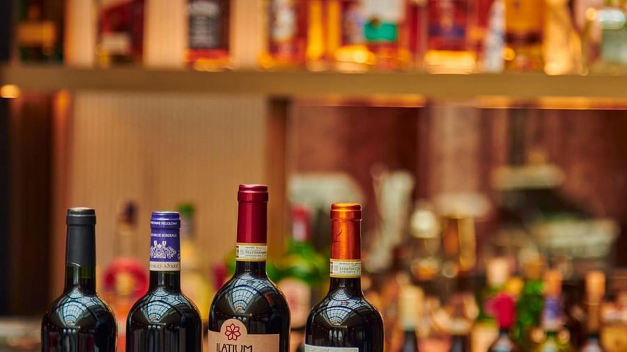 A row of wine bottles is displayed on a glossy bar counter, with shelves of various liquor bottles blurred in the background