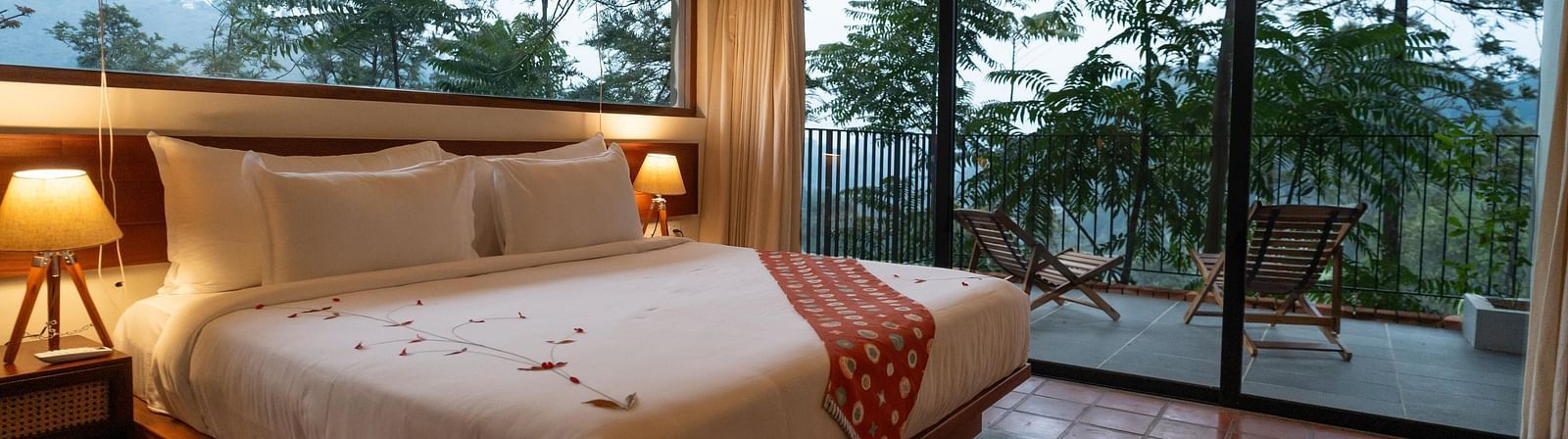  A well-appointed bedroom at Vaasta Vagamon featuring a large bed with a decorative runner, and expansive windows overlooking a scenic view.
