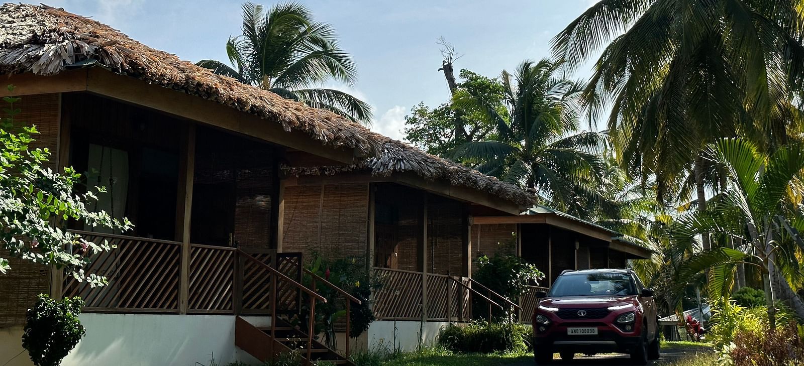 A charming resort building with a thatched roof, surrounded by lush green grass and palm trees under a bright sky.