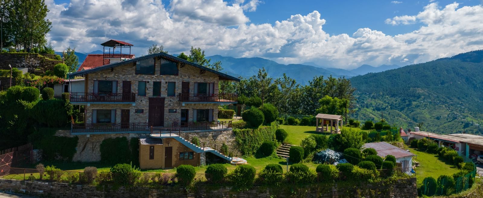 A charming villa surrounded by lush greenery and set against the backdrop of rolling hills and blue skies. - Blusalzz Homes The Himalayan Bungalow, Almora