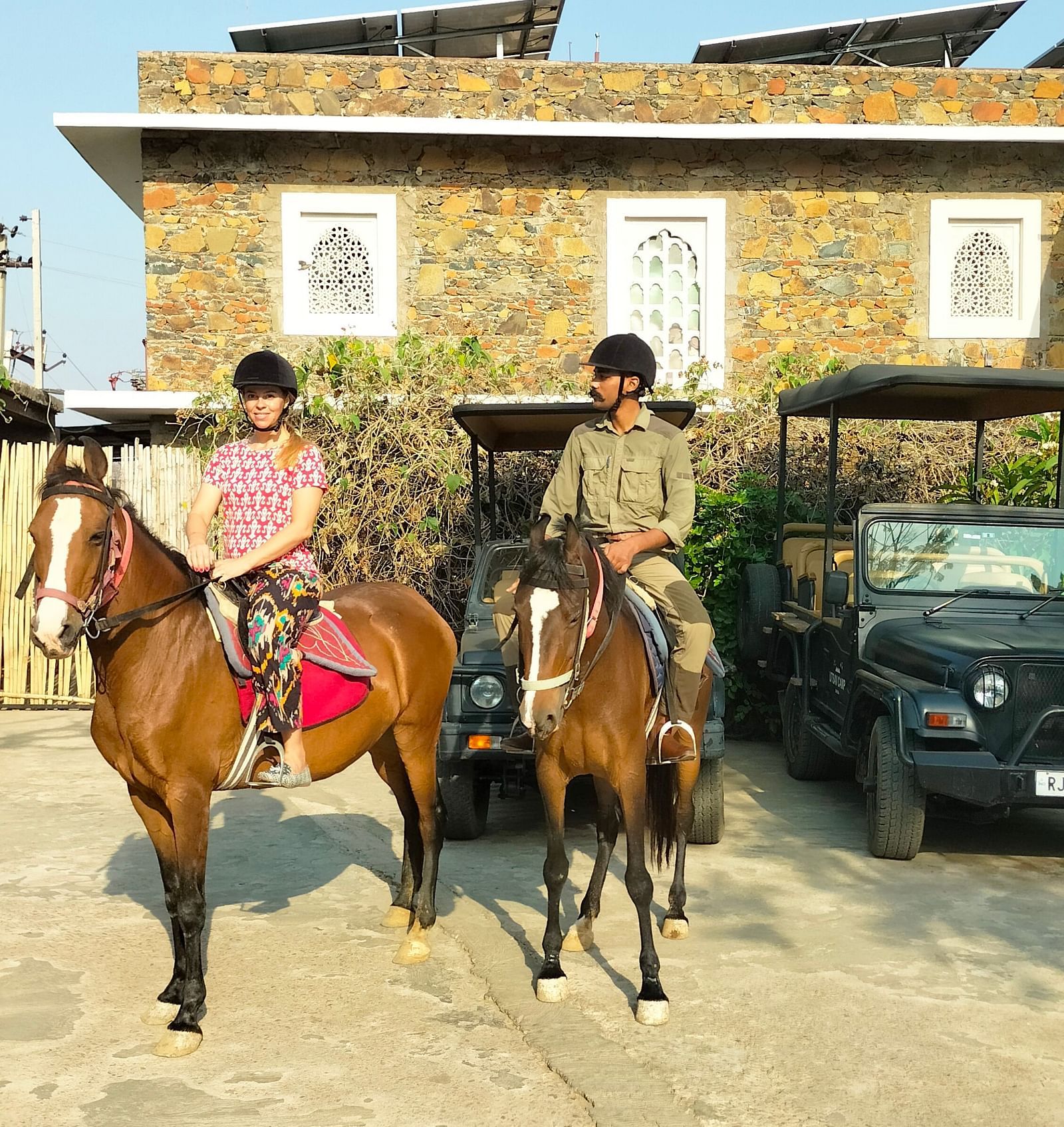 An image of a man and woman riding two horses with the backdrop of the hotel - Utsav Camp Sariska