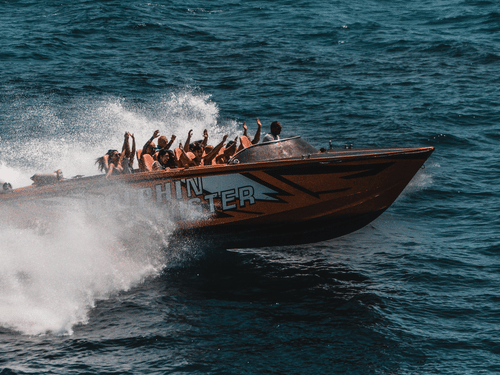A speed boat carrying several passengers, speeding through the dark blue waters.