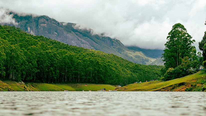 Scenic view of a lake surrounded by lush green hills under a cloudy sky.