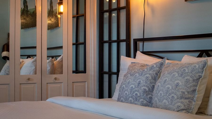 A bedroom with metal headboard, blue patterned pillows, maritime artwork and lantern sconces at Hartstone Inn.