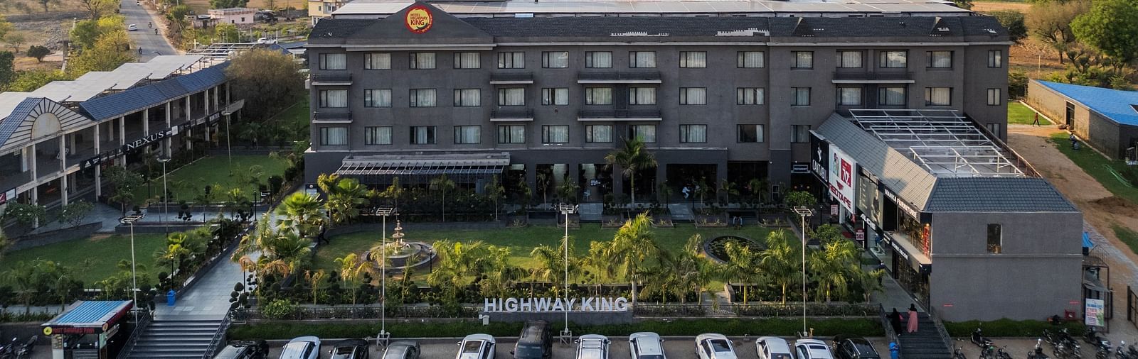 Aerial view of Hotel Highway King, Bagru, with landscaped gardens, parking area, and surrounding buildings in the background.