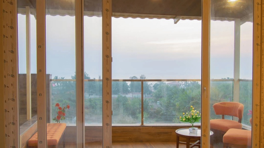 A balcony seating area with orange chairs and a table is seen through glass windows at Estherea Elite, Morjim.