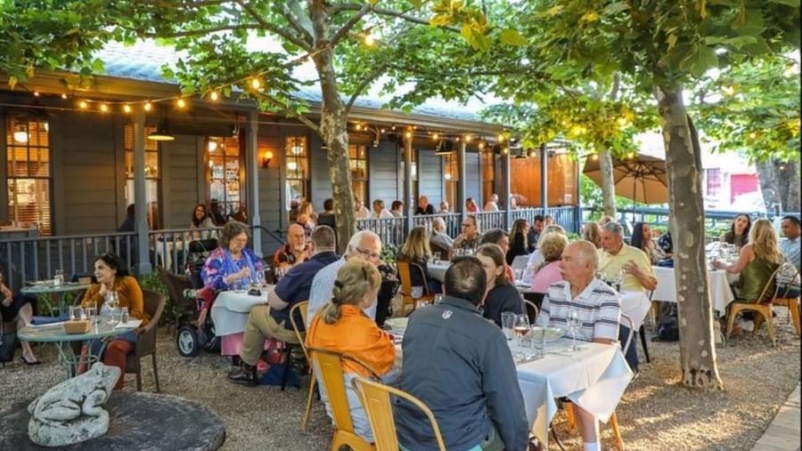 A lively evening scene at the Tallman Hotel's outdoor patio, with many people dining al fresco.