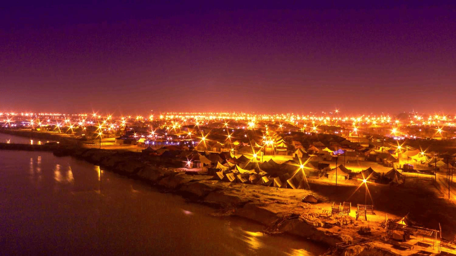 Night view of Prayagraj city with illuminated buildings and riverfront, showcasing the cityscape