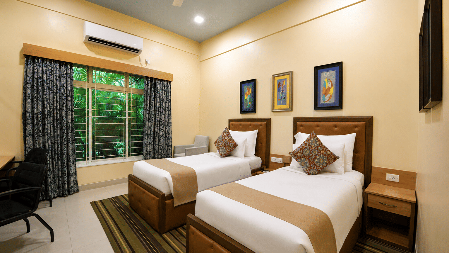 Executive room with two single beds, tan leather headboards, framed artwork, a work desk, chair and a striped rug at MAYFAIR World Cup Village, Rourkela.