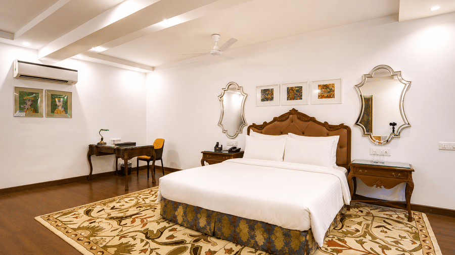 Deluxe suite bedroom with a king bed, tufted headboard, bedside tables, framed artwork, mirrors, writing desk and a floral rug at MAYFAIR Garden, Rourkela.