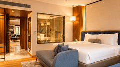 Guest room at Pride Premier Pune featuring a king-size bed, blue armchair and open layout with warm lighting.