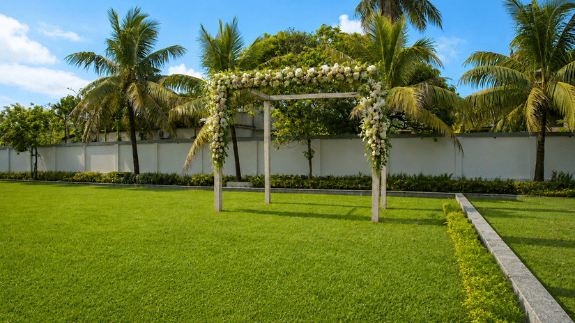 A wedding mandap frame decorated with white floral garlands set up on the lawn at Pride Elite Mandarmani, surrounded by coconut palms.