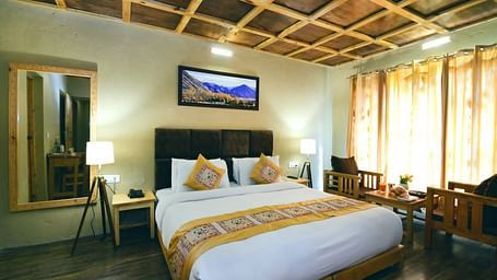 Standard Cottage with a king size bed, a TV, a mirror, and a wooden ceiling at White Sands Resort, Ladakh.