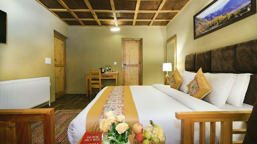 Standard Cottage featuring a king size bed with white linens and a yellow runner, flanked by wooden bedside tables at White Sands Resort, Ladakh.