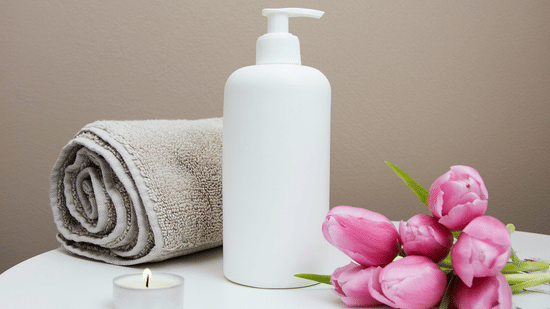 A bunch of tulip flowers kept next to a bottle and a rolled towel by a tealight candle