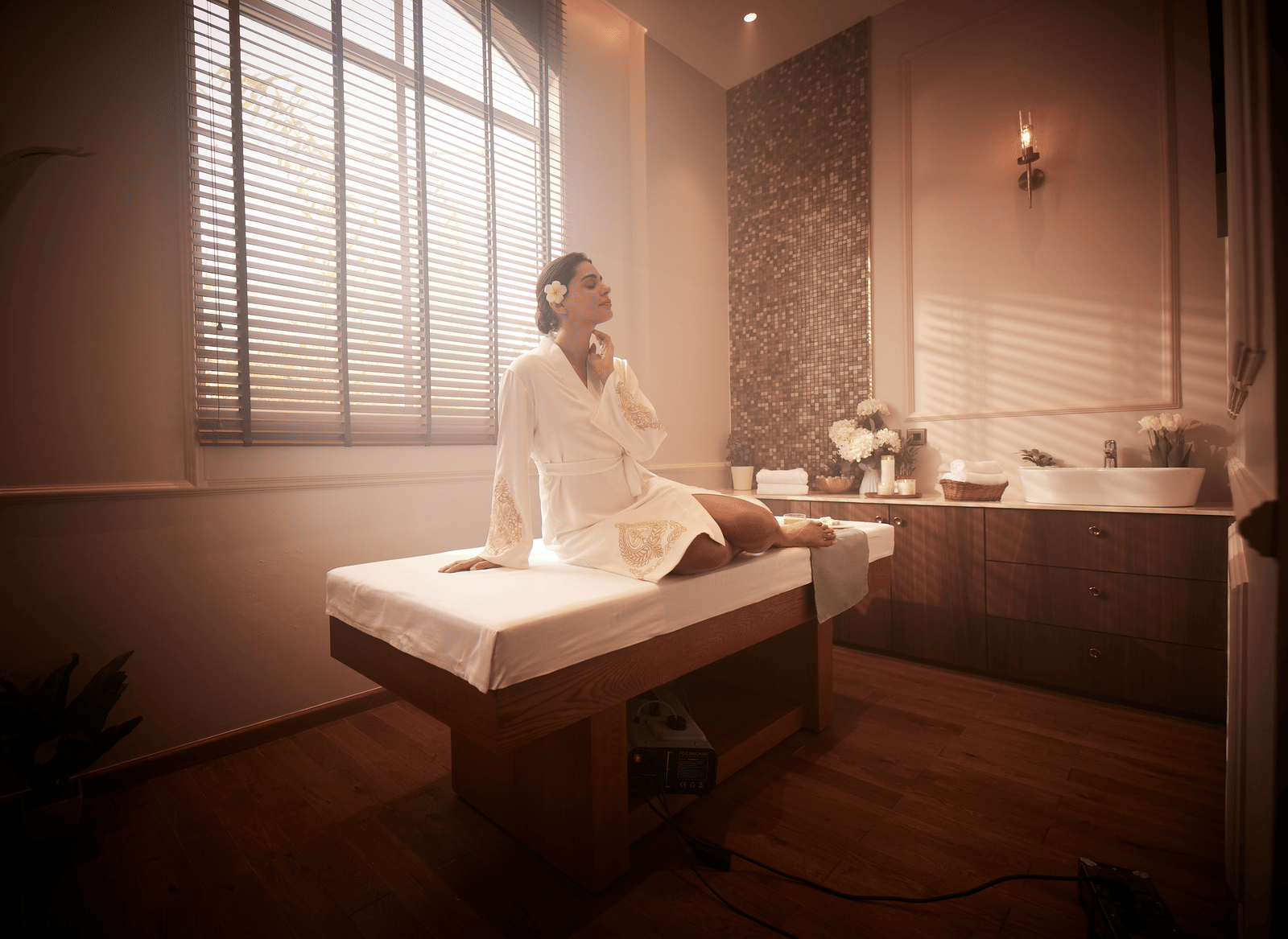 A woman sitting in an upright position on a spa bed with natural light coming from the window behind her.