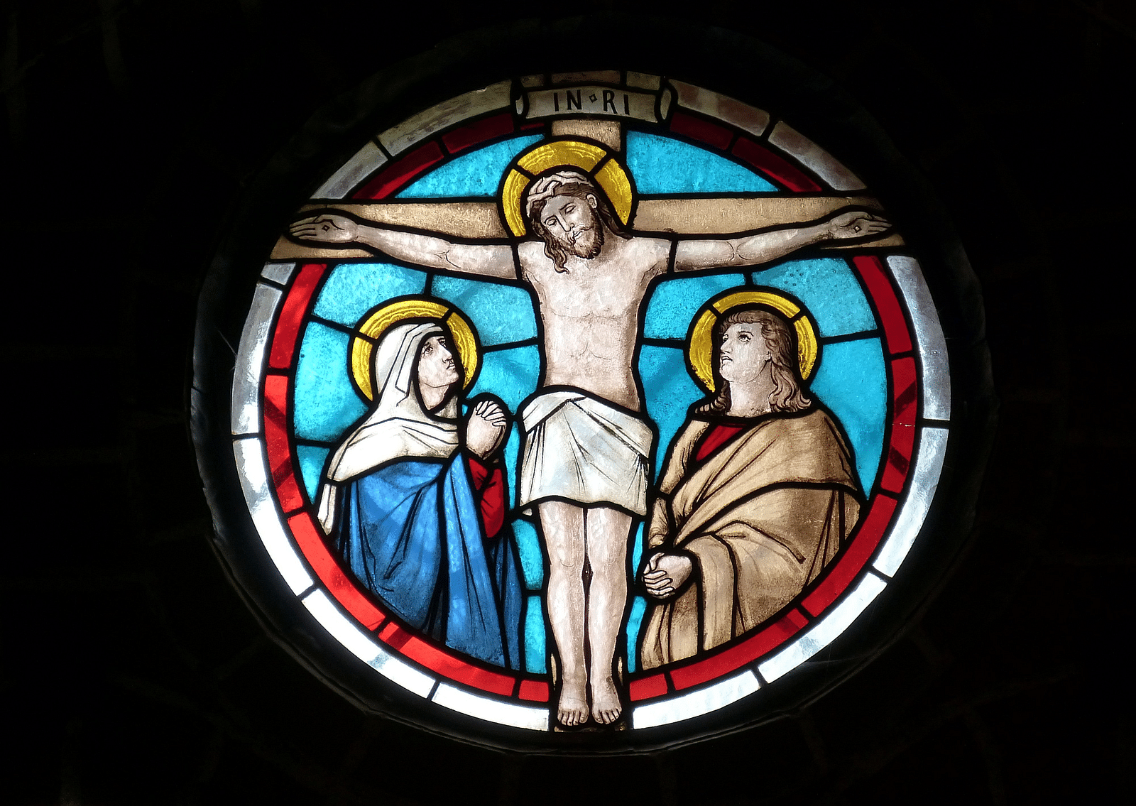 An overview of a stained glass inside a church depicting christ on a cross.