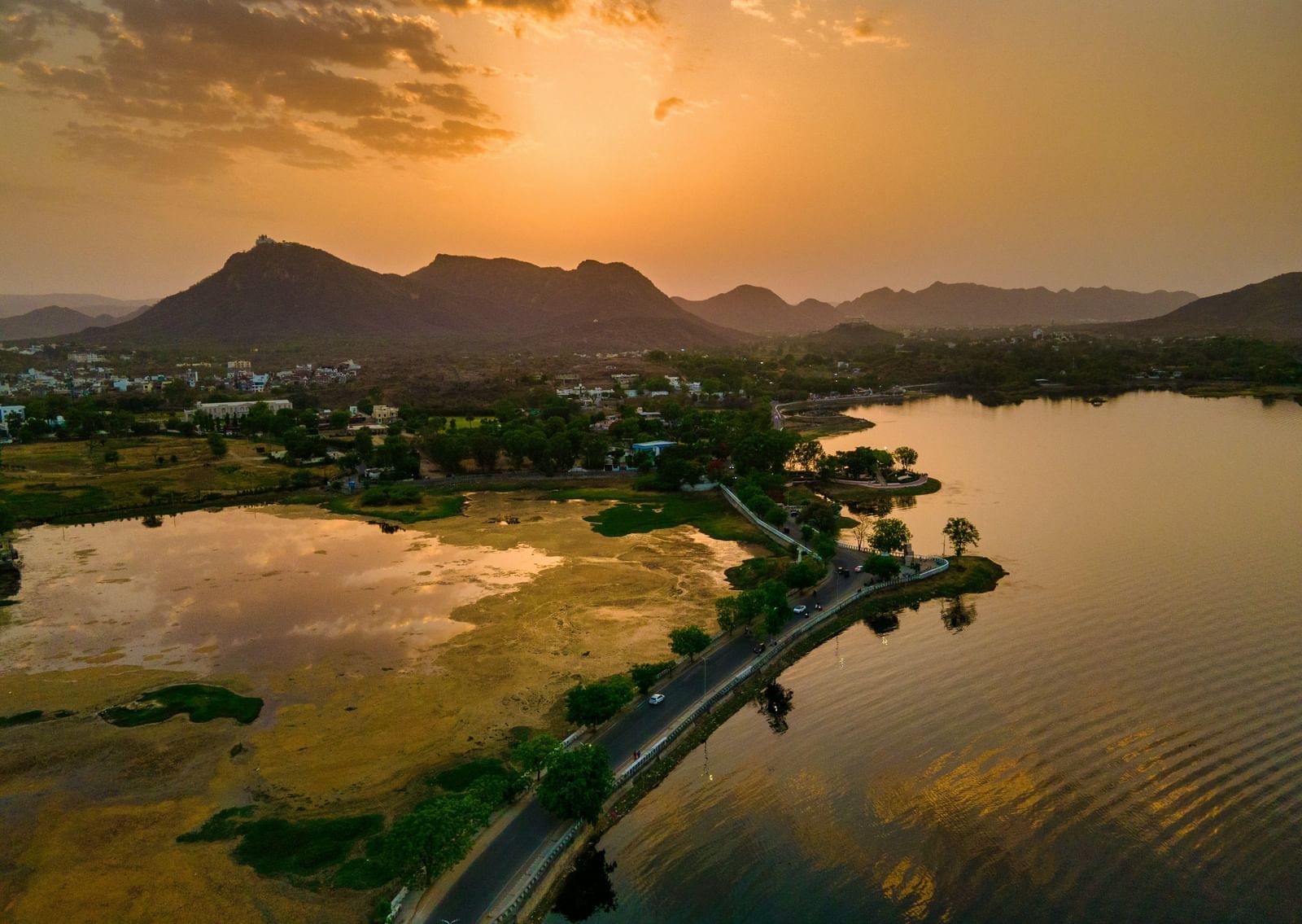 An aerial view of Fateh Sagar Lake with mountains in the background and the sun setting as well.