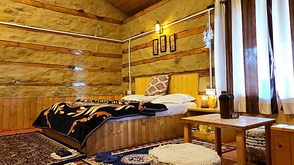 Corner-view shot of the Indrasan Peak Cottage with a window covered with thin curtains beside it at Amara Upepo - The Sky Village, Manali.