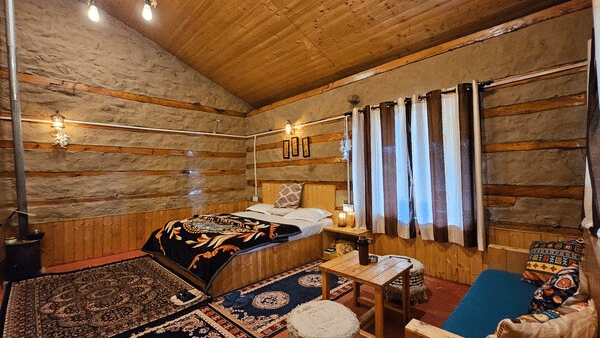 Full view of the Indrasan Peak Cottage featuring a double bed in the corner along with a cosy seating area at the Amara Upepo - The Sky Village, Manali.