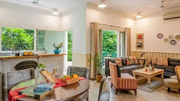 Cosy dining area with rustic wooden furniture, colourful cushions, and windows opening to a green view at Karma Chalets.