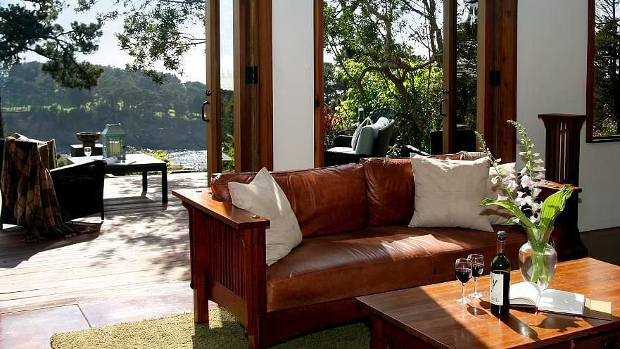 Sunlit lounge area with a red leather couch, wooden table with flowers, and open doors leading to nature - Brewery Gulch Inn & Spa