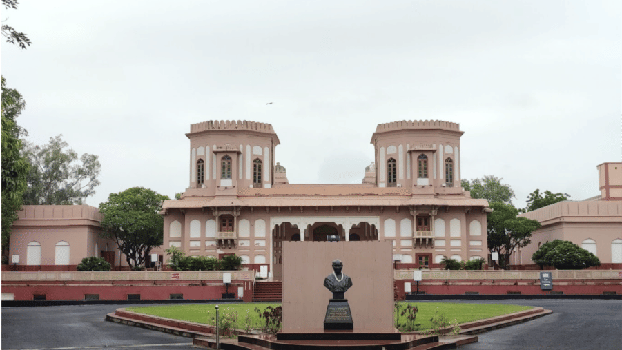 An exterior view of Sardar Vallabhbhai Patel National Memorial featuring 2-storey circular towers, a centrally positioned stone statue surrounded by manicured lawn, and clear sky.
