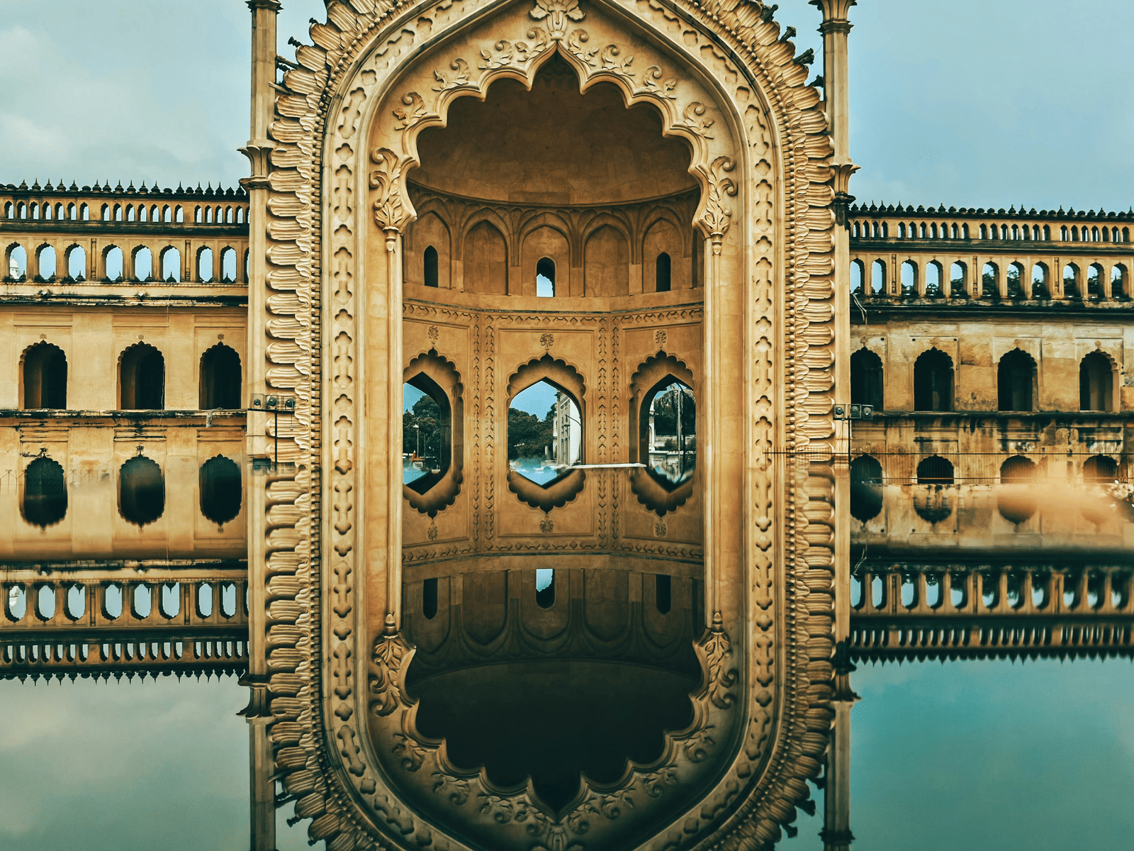 A detailed, arched gateway with two large, circular windows is reflected in a still body of water.