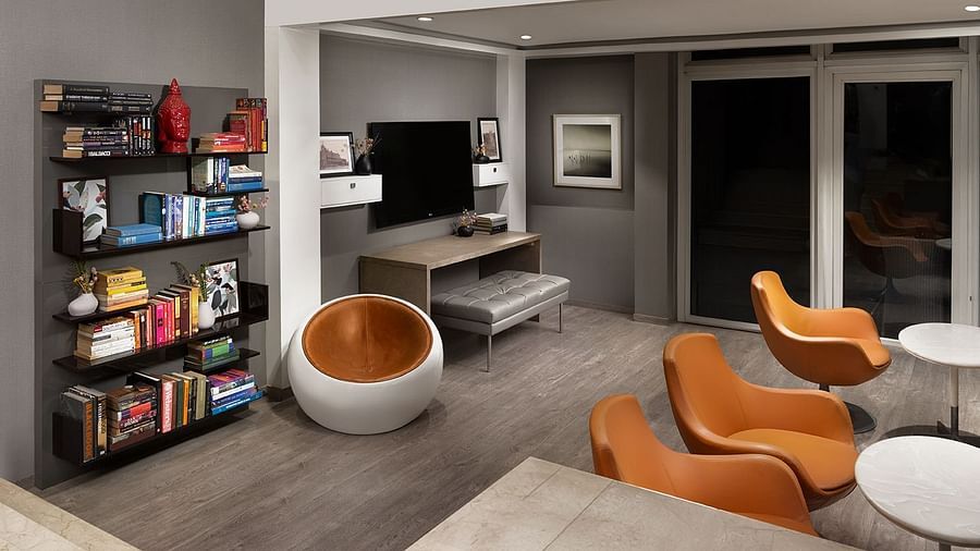 A spacious, modern multi-level living area at The Atara, Gurugram features an upper mezzanine level, a large bookshelf, a comfortable sofa, and a stylish armchair, creating an open design