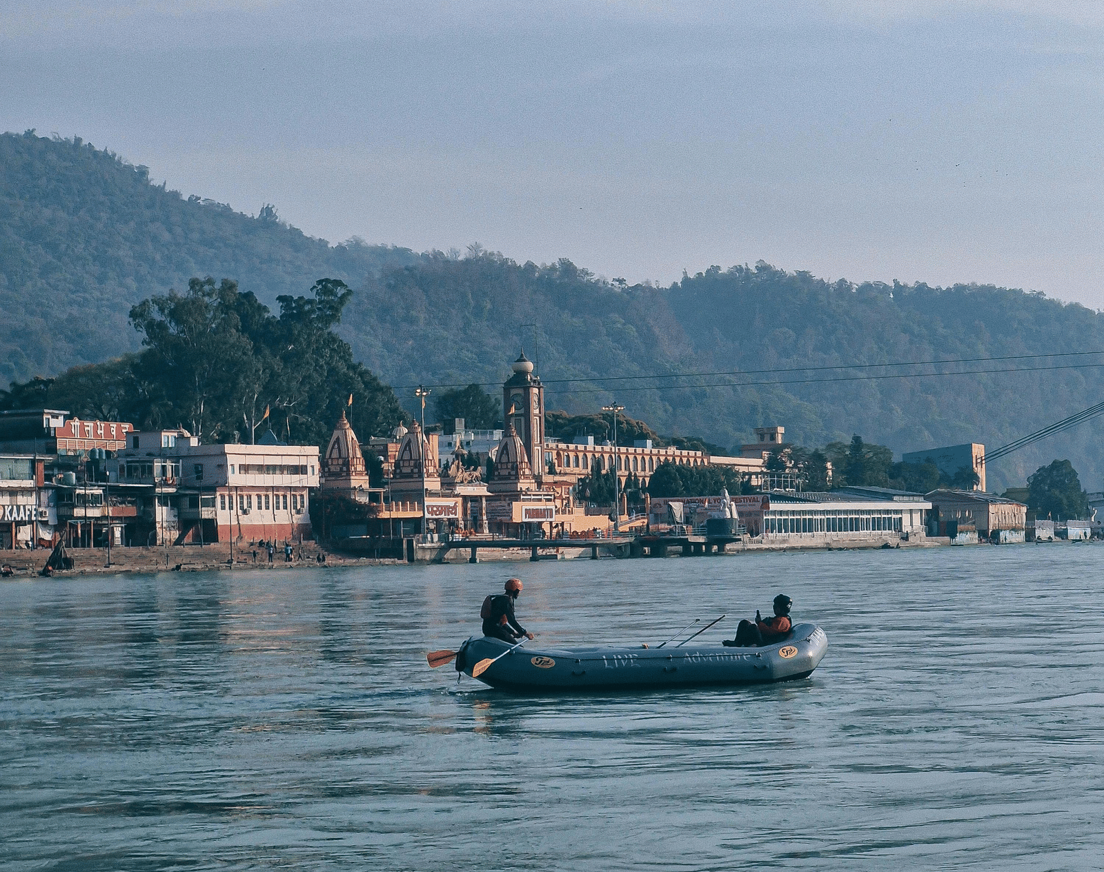 Boat gliding on the Ganges River in Haridwar, with temples and hills forming a serene backdrop under a clear blue sky.