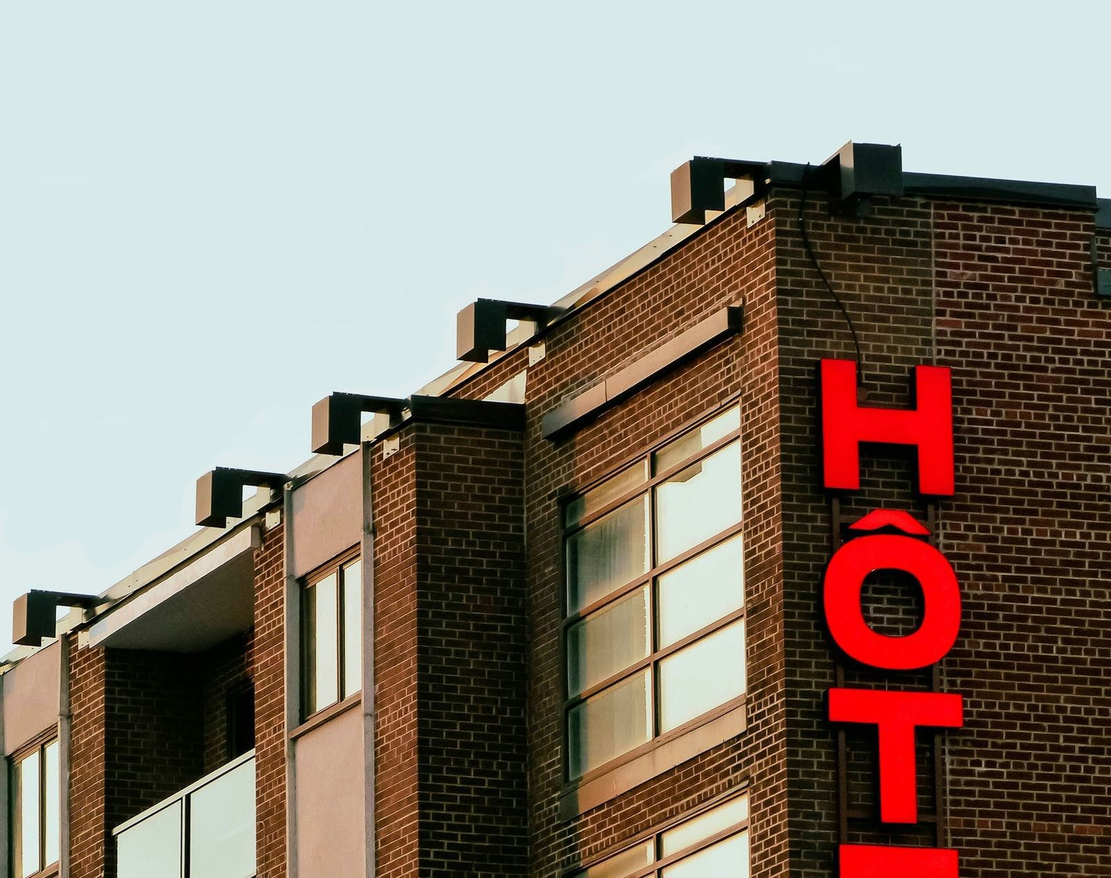 Close-up of the upper floors of an older, dark brick building with a vertical, bright red neon sign spelling out the word 'HOTEL'.