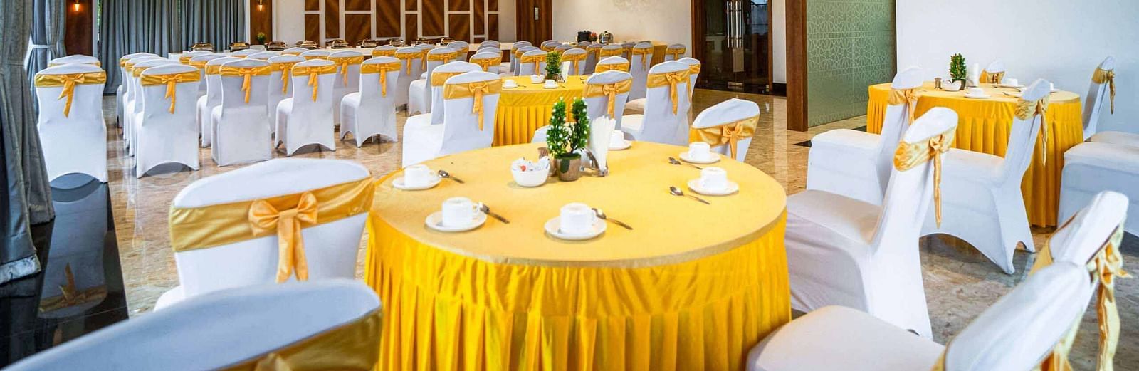 A brightly lit banquet hall at Mansha Palace is elegantly prepared for an event with round tables and draped chairs.