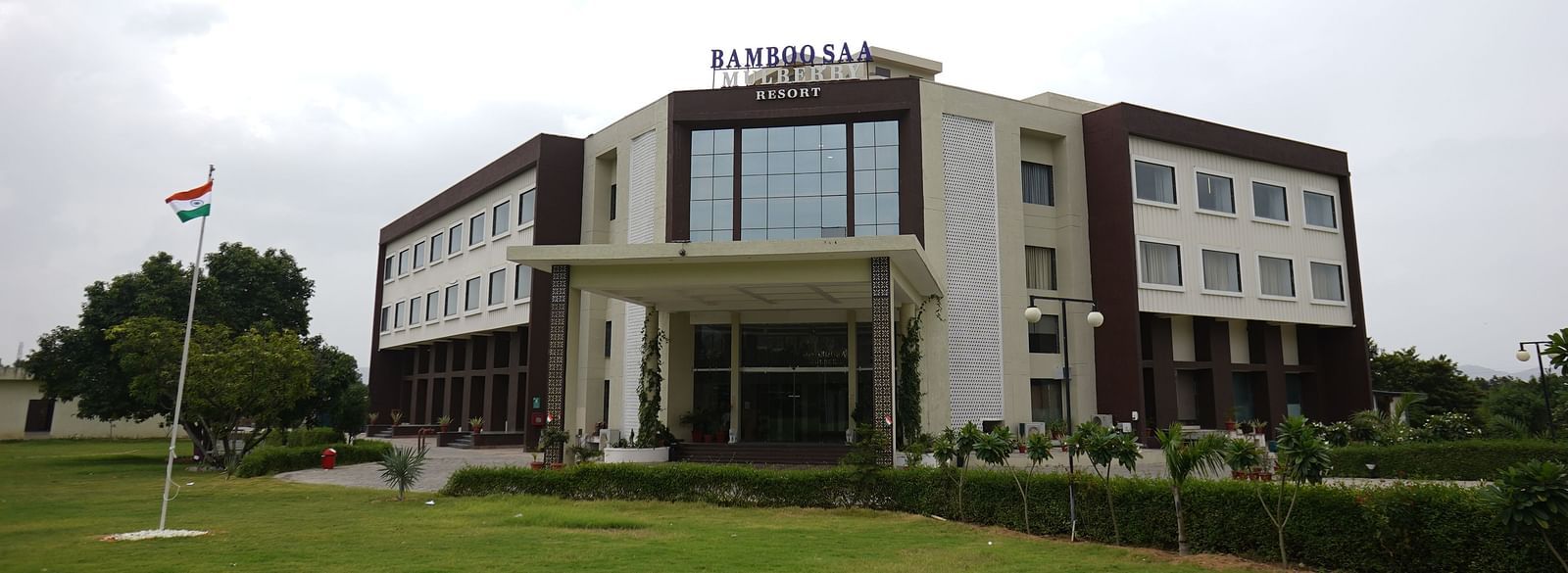 Exterior view of Bamboo Saa Mulberry Resort, Pushkar, Rajasthan featuring a modern building with a light-coloured facade with a lawn in the foreground