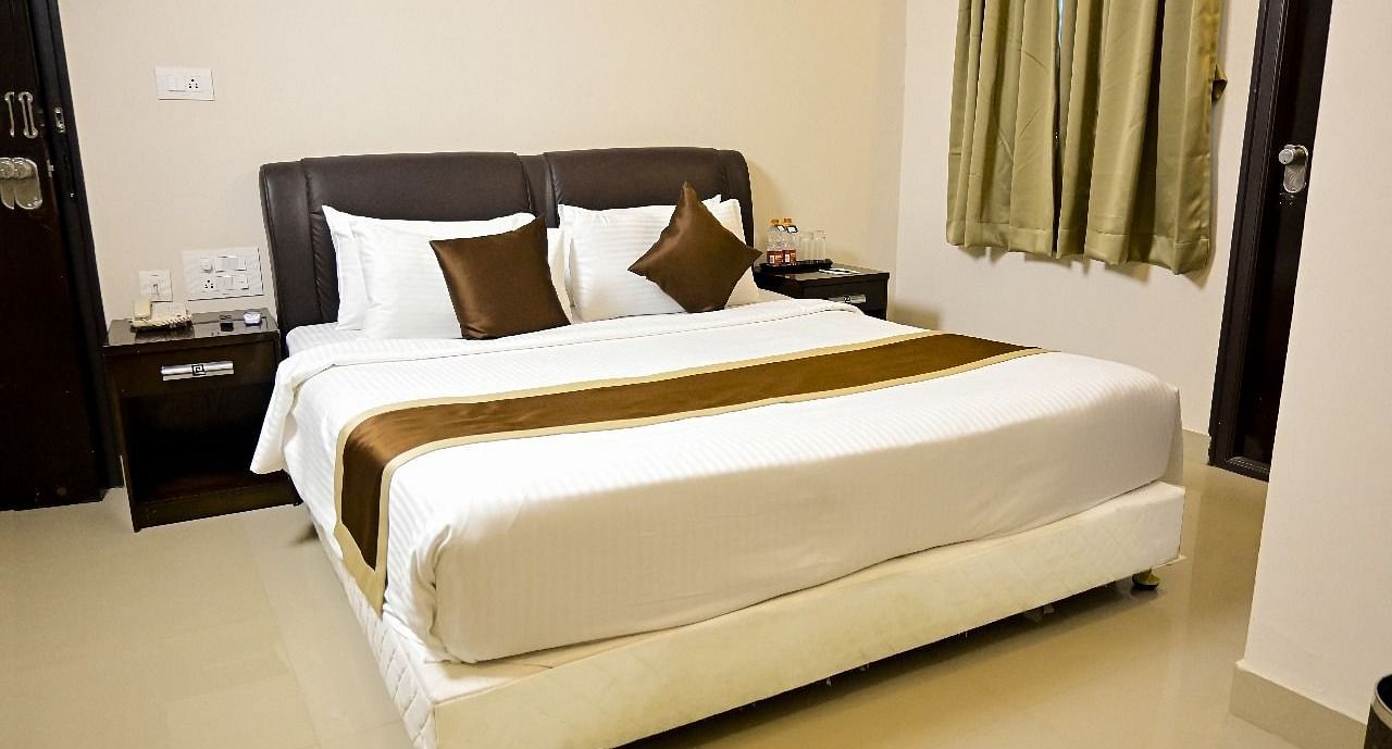  A comfortable hotel room at TGI Livancia Hillside, JC Nagar, Mysore, with a neatly made double bed, bedside tables with lamps, and curtains on the window.