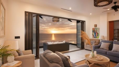 A modern living room with large sliding glass doors opening to an outdoor patio with a view of the sunset.