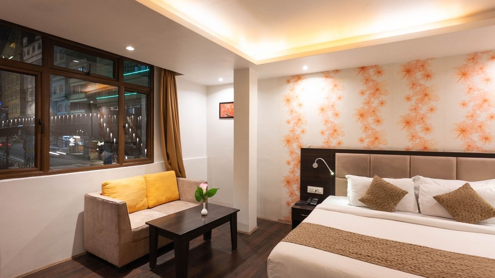 Deluxe Room at Avianna Hungry Jack, Gangtok featuring a plush bed next to a sitting space with a two-seater sofa and a coffee table by the window under warm lighting