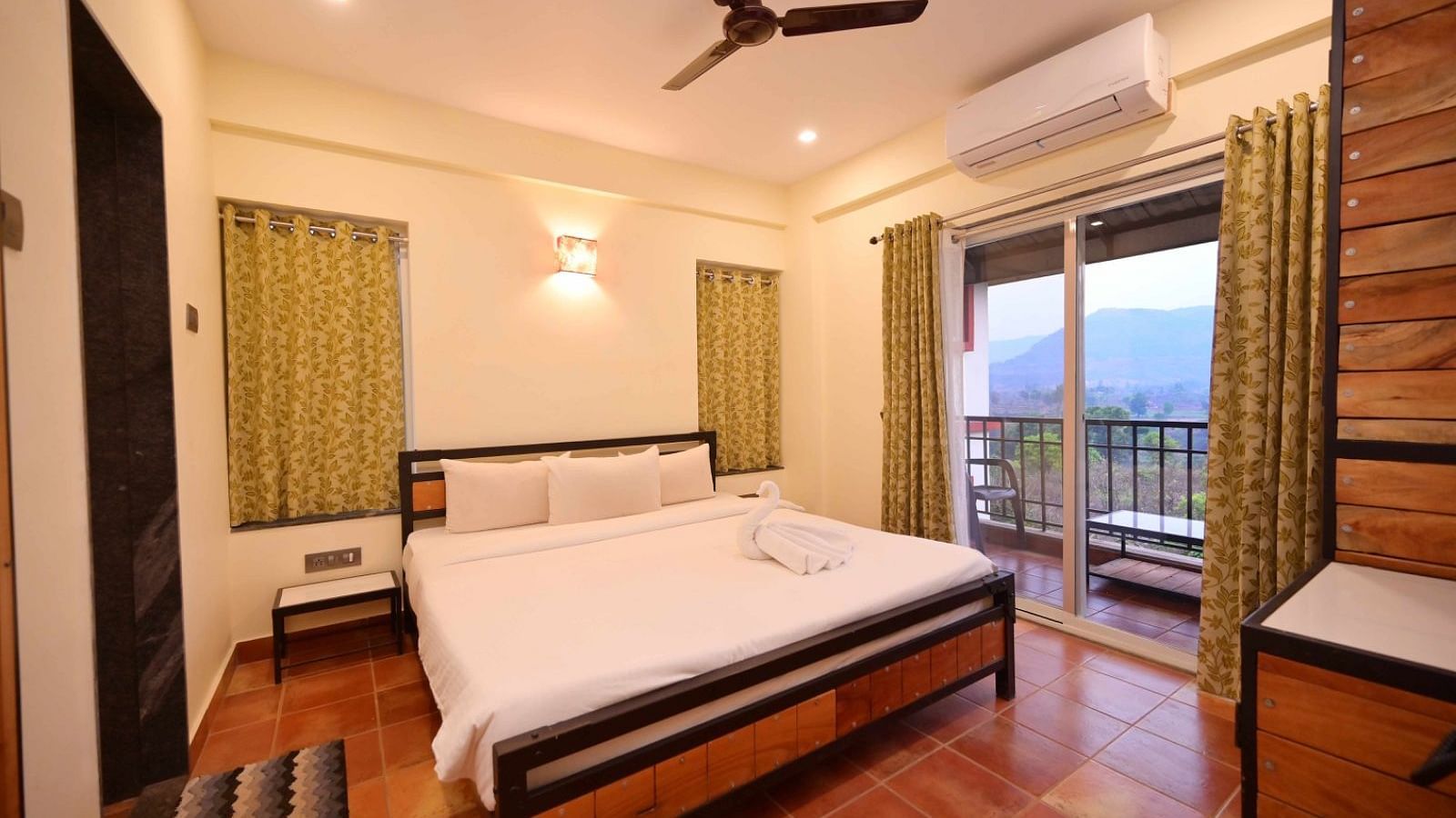 A bedroom with a wooden bed frame, white linens, and a balcony with a view of trees