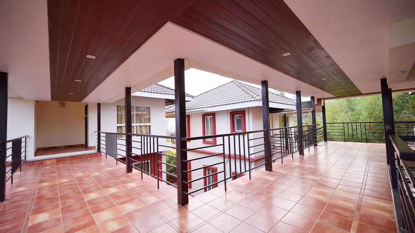 A partially covered outdoor walkway with tiled flooring, black railings, and a view of a building with white walls and red accents.
