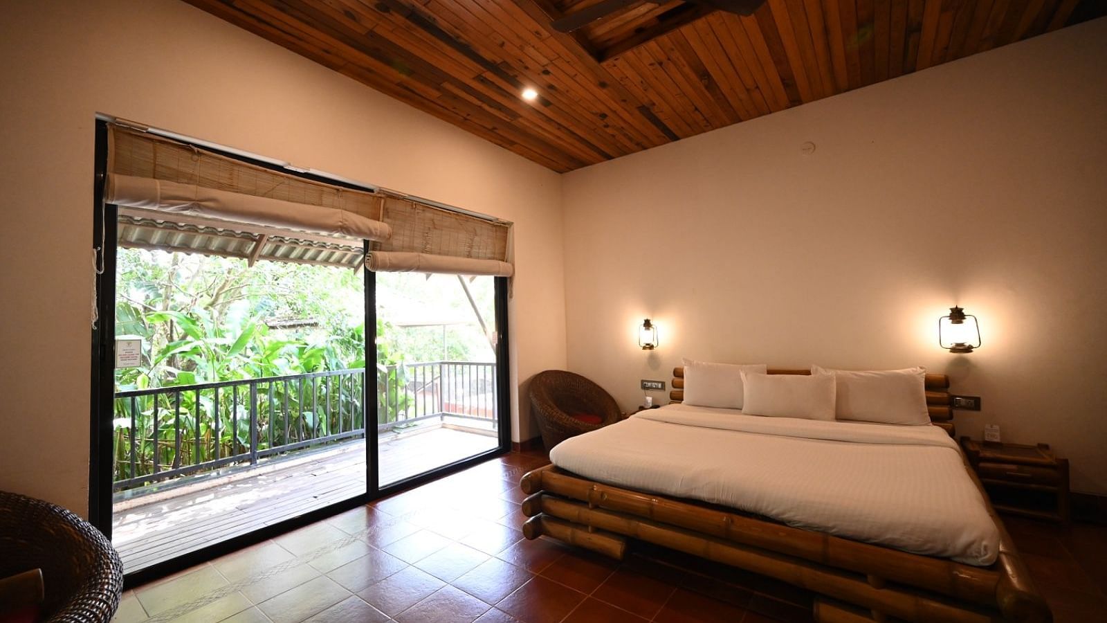 A bedroom with a wooden bed frame, white linens, and a window with a view of trees.