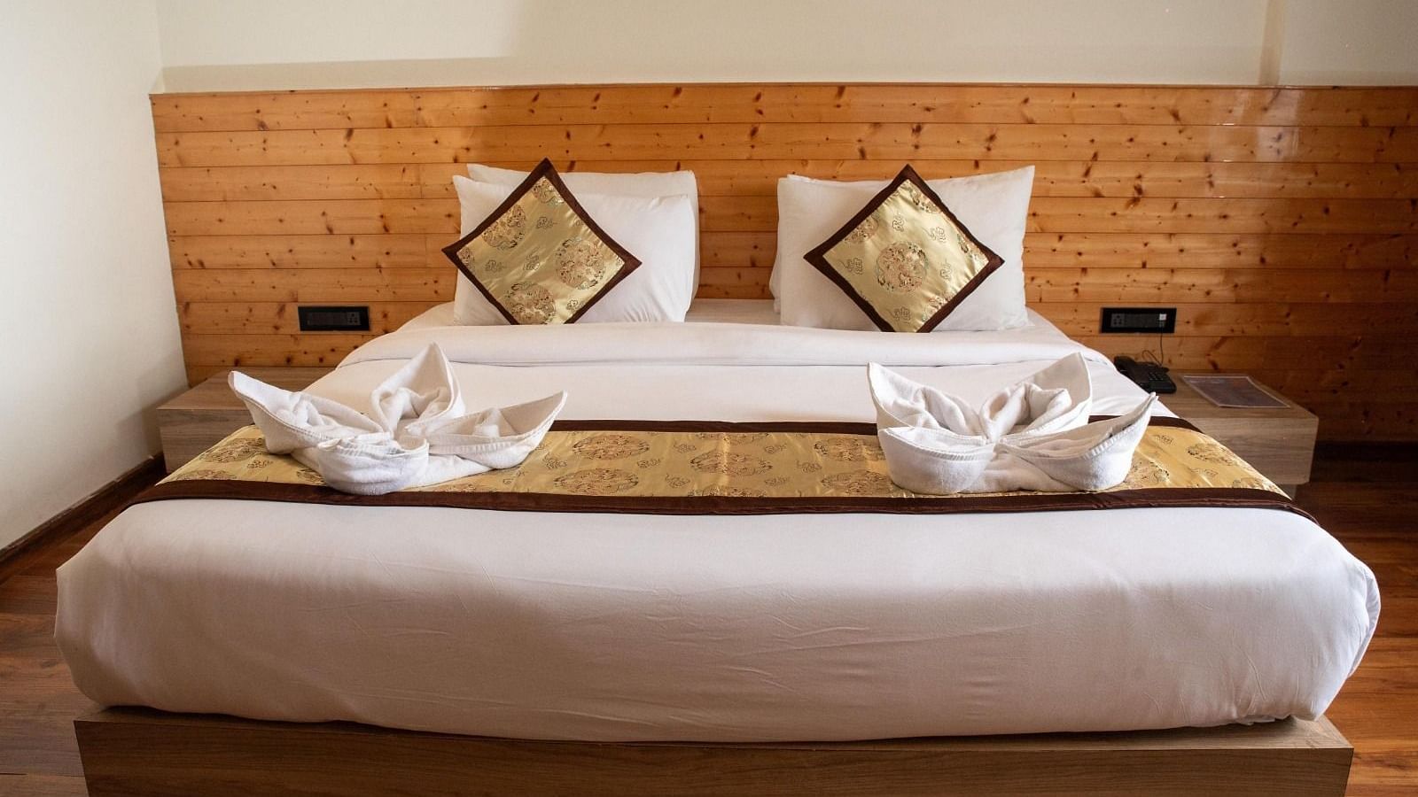 Front view shot of a double bed with well-arranged pillows and cushions along with two bed side tables on either side of the bed at Sumitel Sanderling.