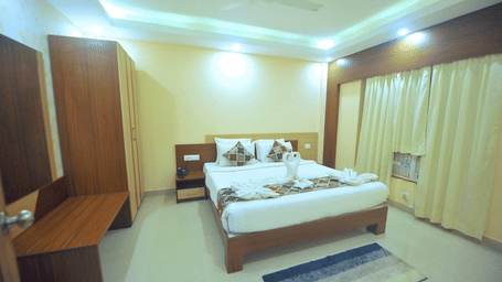 A neatly made double bed with decorative towel art inside a brightly-lit bedroom at Pipul Hotel And Resort, Puri.
