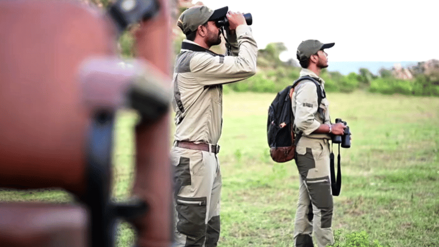An image of two men viewing the mountains - An image of a jeep parked amidst the rocky mountains - Utsav Camp Sariska
