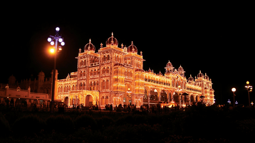 Facade of the Mysore Palace lit up at night and people walking around