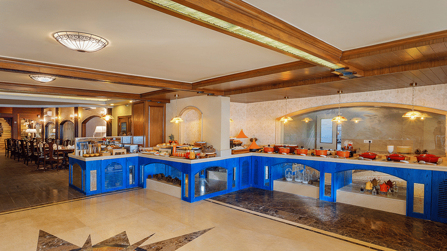 A buffet spread with serving stations and food displays linig a dining room at Ramada by Wyndham Mussoorie Mall Road.