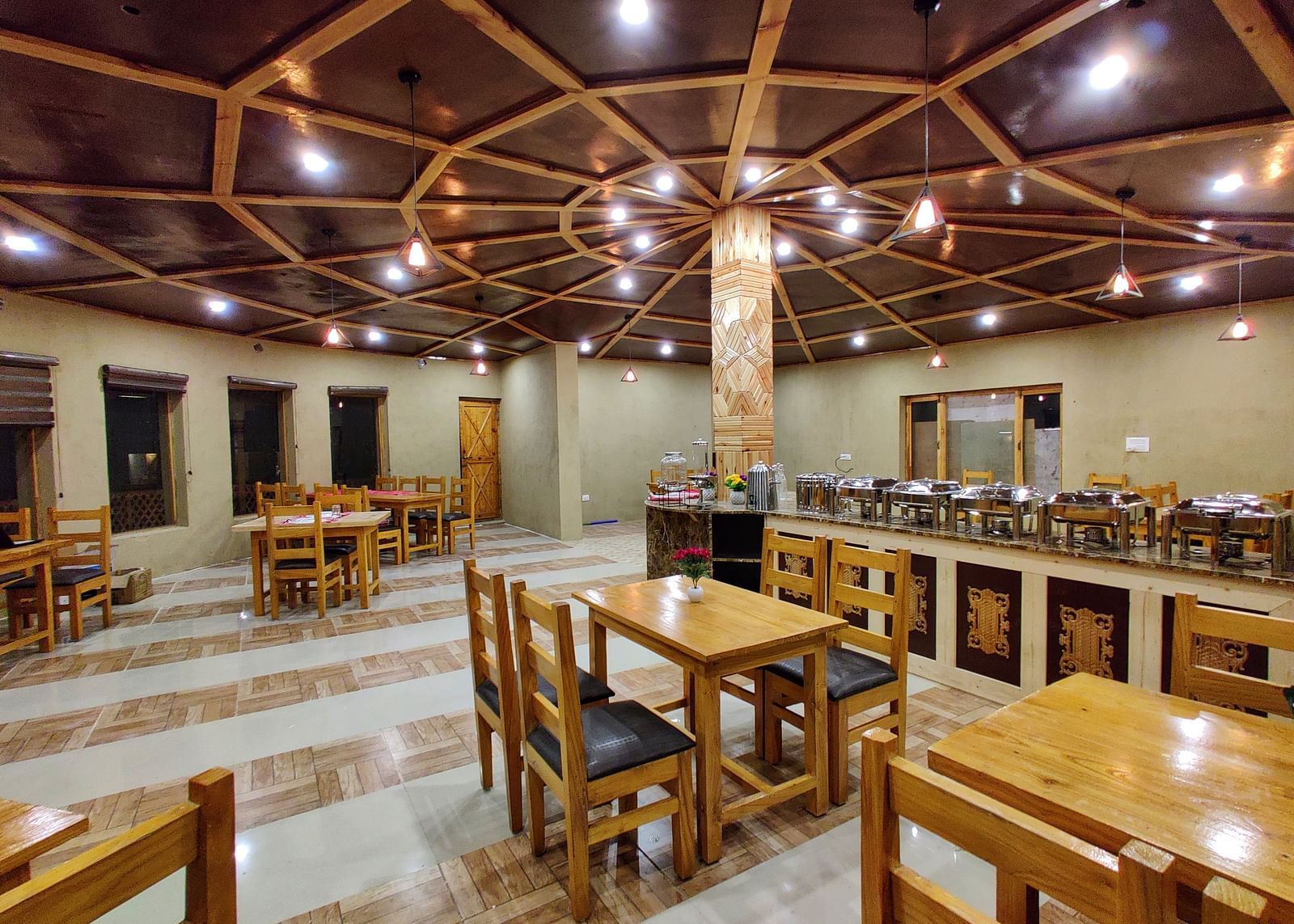The interior of a dining area at White Sands Resort, Ladakh highlighting the wooden furniture, ceiling design, and buffet area.