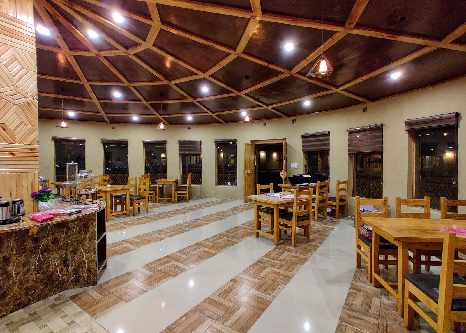 The interior of a dining area at White Sands Resort, Ladakh, with wooden tables and chairs, a buffet setup in the background, and decorative lighting fixtures.